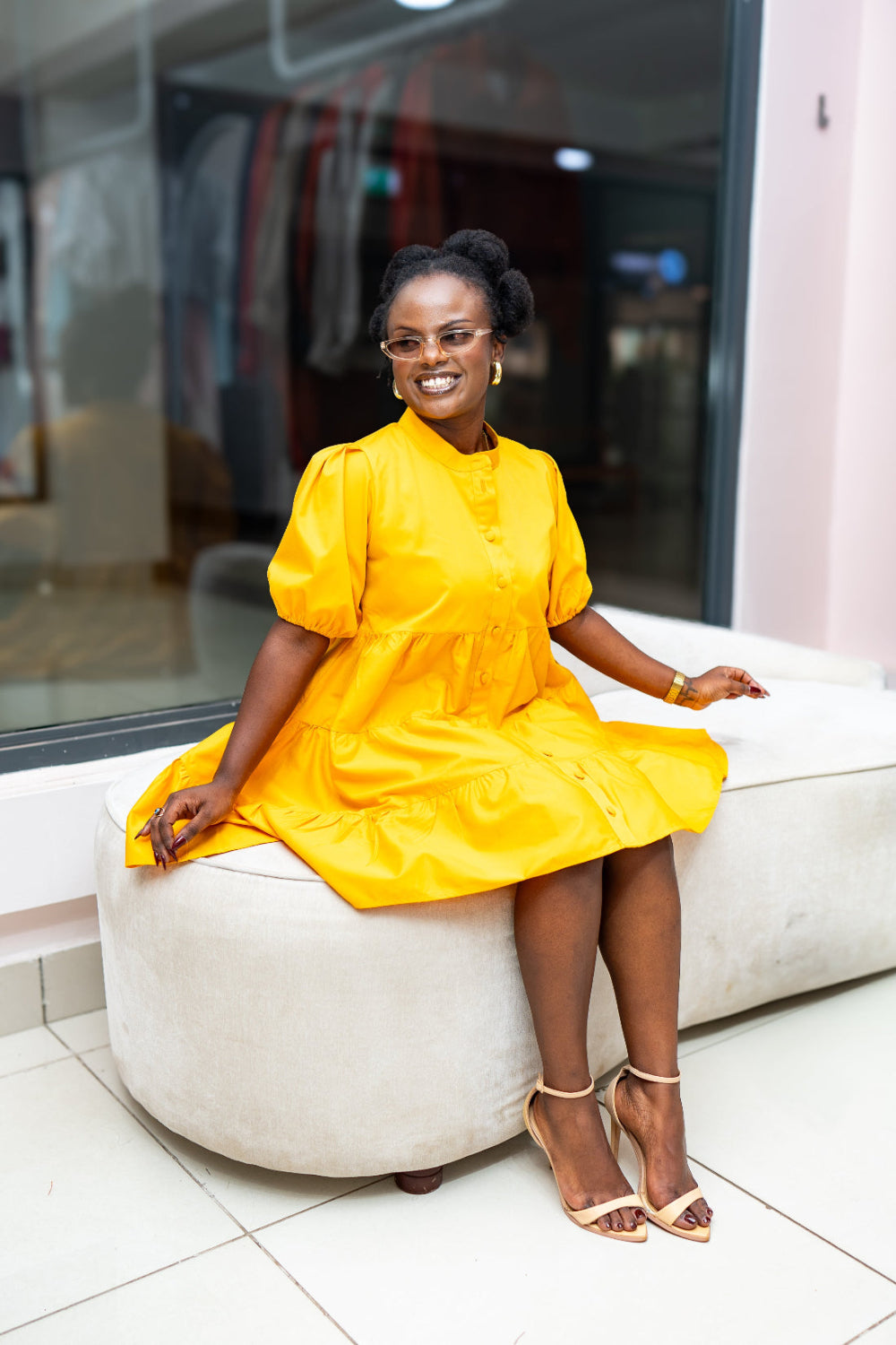 Woman in a yellow dress sitting on a white couch in an indoor setting.