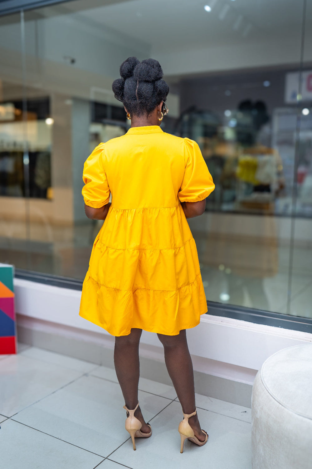 Person wearing a yellow dress standing in front of a glass wall.
