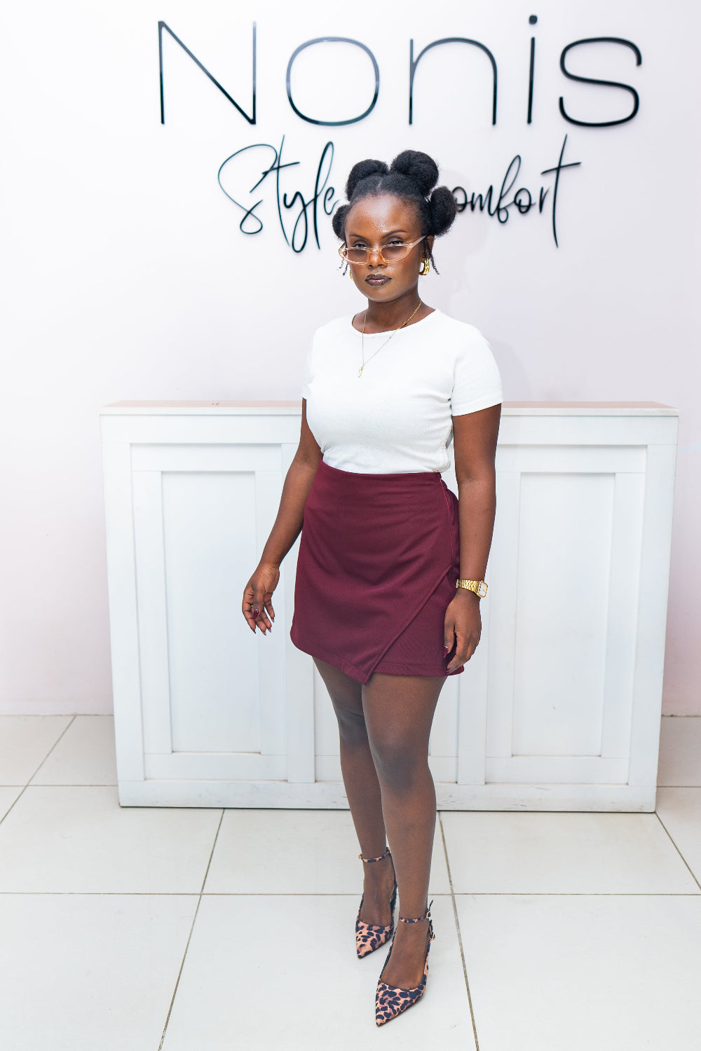 Woman in a white top and maroon skort standing in front of a white wall with 'Nonis Style Comfort' text.
