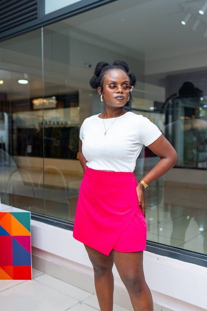 Woman in a white top and pink skort standing in front of a glass wall.