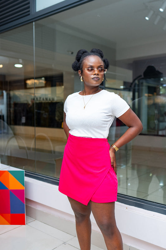 Woman in a white top and pink skort standing in front of a glass wall.