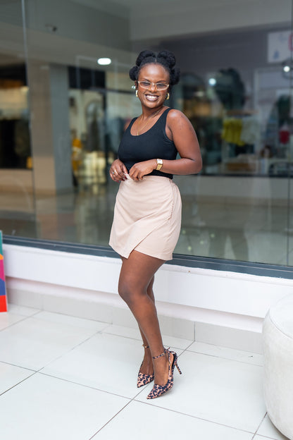 Woman in a black top and beige skirt standing in a shopping mall.